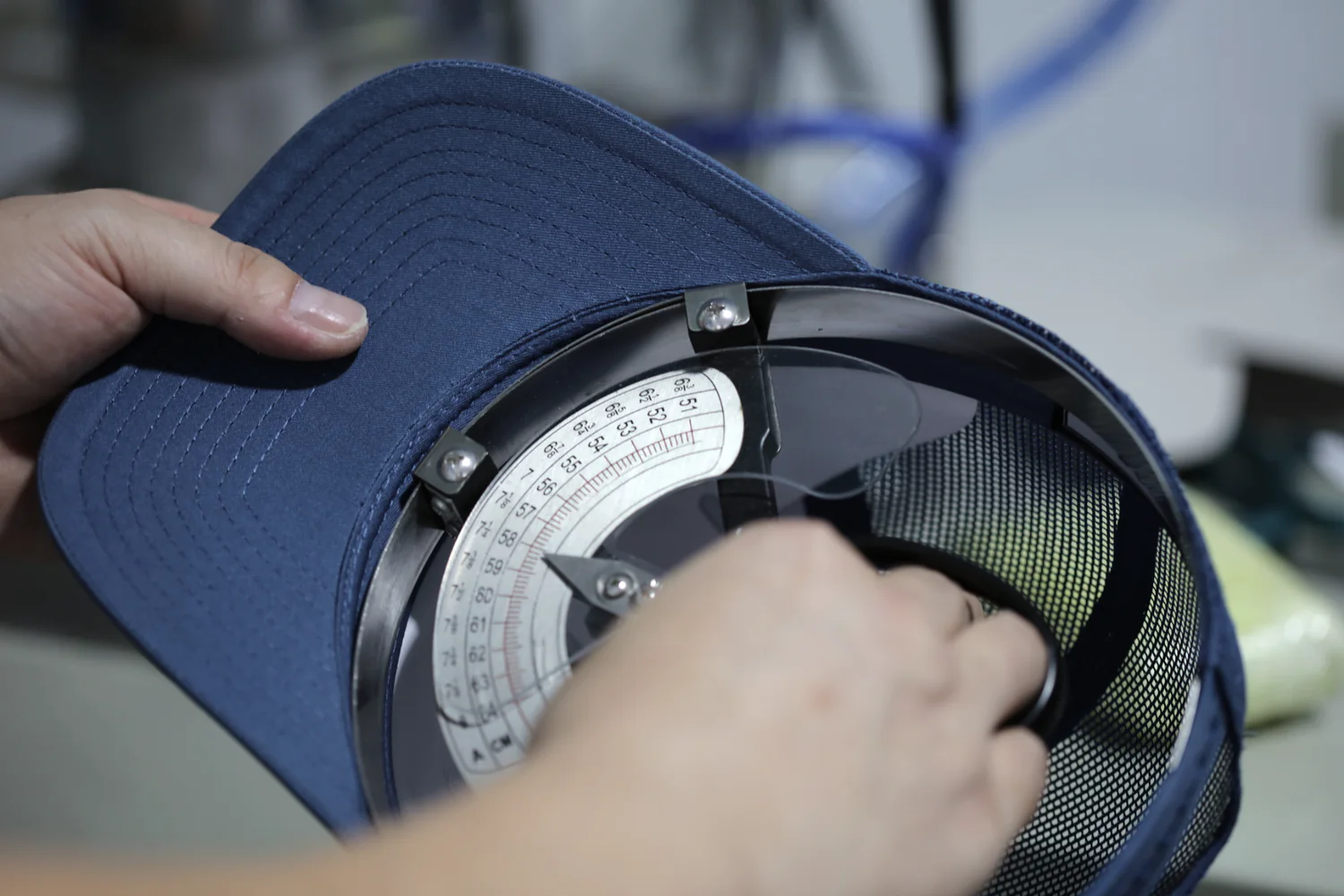 Inspector measuring the inside circumference of a blue trucker cap with a cap-sizing gauge.