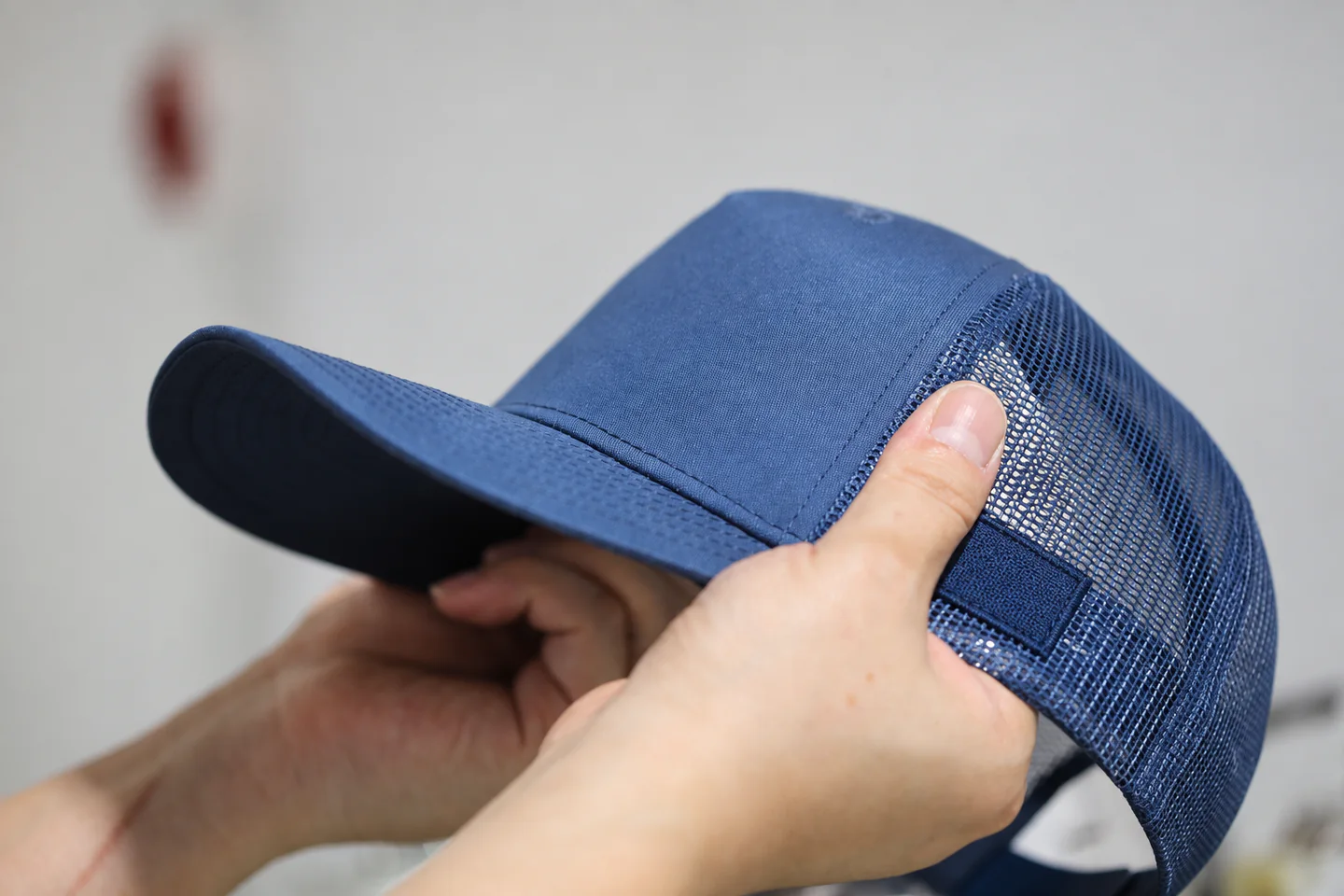 Inspector checking the placement and edge stitching of a plain woven side patch on a blue trucker cap.