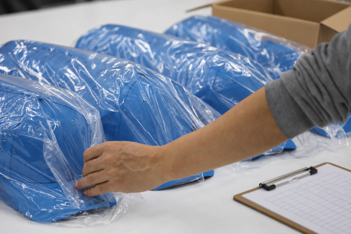 Worker reviewing individually bagged blue caps beside a packing checklist and open carton.
